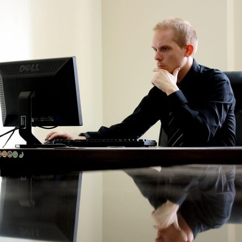 A Man Sat Working At A Computer Monitor