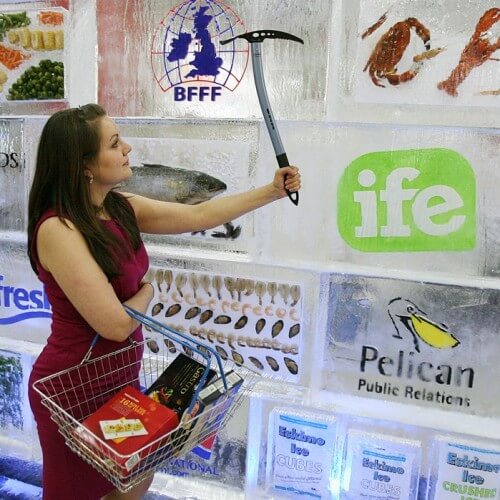 A Woman Using A Pick On An Ice Wall With Logos In It