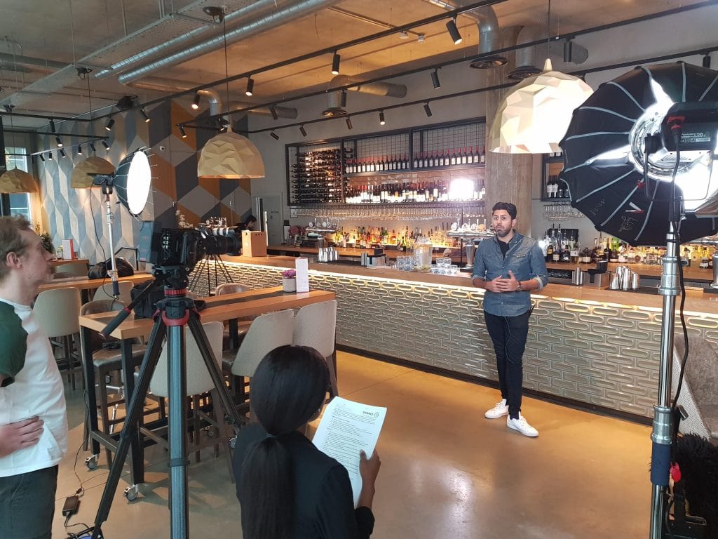 A Man Being Filmed Presenting In Front Of A Bar