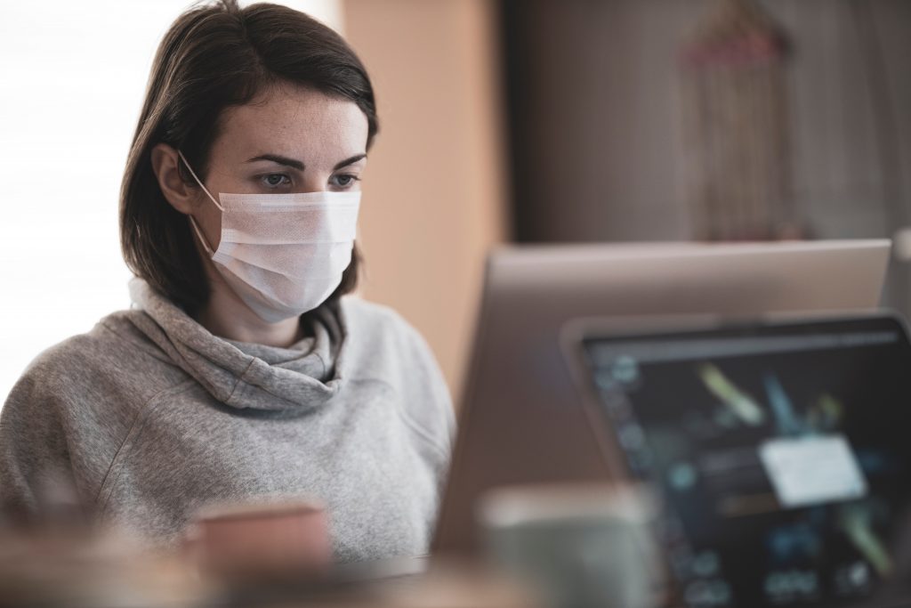 A Woman Working On A Laptop Wearing A Face Mask